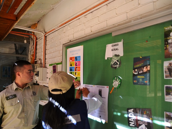 La facilitadora intercultural de la Defensor&iacute;a, Andrea Mamani, y el cabo de guardia fijan el afiche de derechos en el diario mural del cuartel. 
