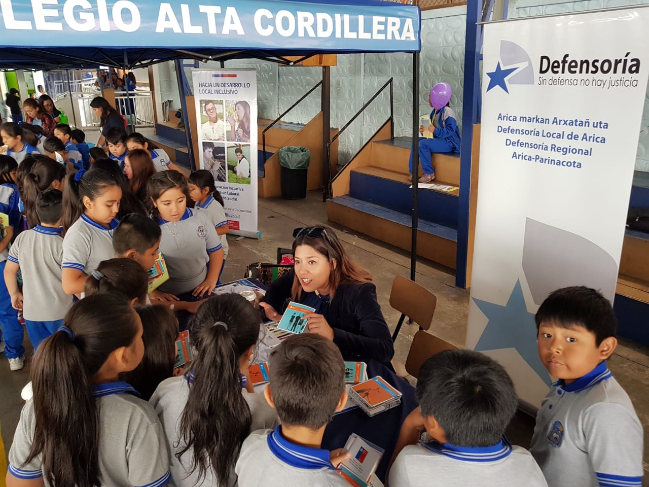 La encargada de comunicaciones de Arica, Daniela Tapia, junto a alumnos del Colegio "Alta Cordillera" que reciben folleter&iacute;a de la DPP.